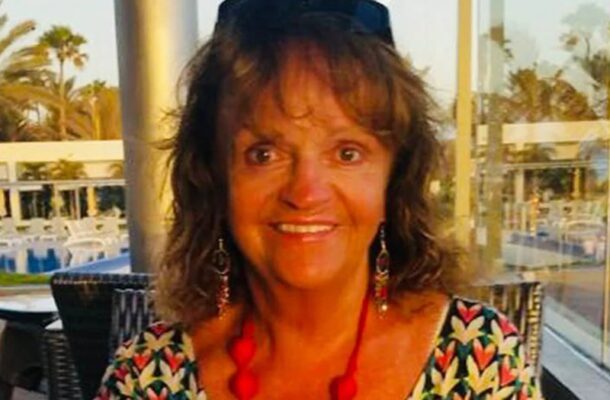 Smiling woman with shoulder-length brown hair wearing a colorful patterned top and a red bead necklace at an outdoor cafe.