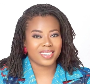 Portrait of a smiling woman with dreadlocks and red earrings, wearing a blue patterned blazer.