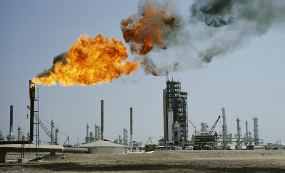 Industrial oil refinery with gas flares shooting orange flames and dark smoke above a desert-like facility