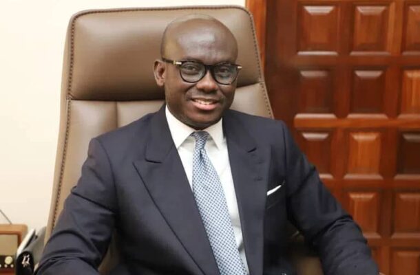 Godfred Yeboah Dame | Ghanaguardian.com Man in a navy suit and light blue tie sits in a brown leather office chair, smiling at the camera.
