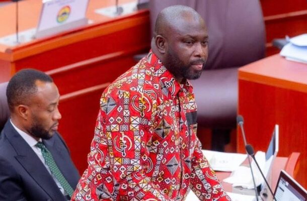 Man in a red patterned shirt speaks at a podium in a formal meeting room, with a colleague seated beside him.