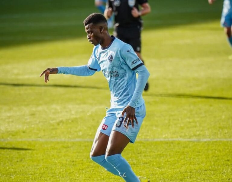 Soccer player in a light blue kit dribbling on a sunny green field