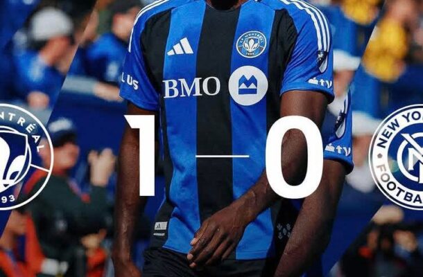 Soccer player in blue and black striped jersey walking on the field with a bold 1–0 score overlay, crowd in the background, team crests and sponsor logos visible.