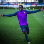 Footballer in a purple FC Barcelona training kit celebrates with arms outstretched on a grassy field, a 'COMUNICAT MÈDIC' banner above.