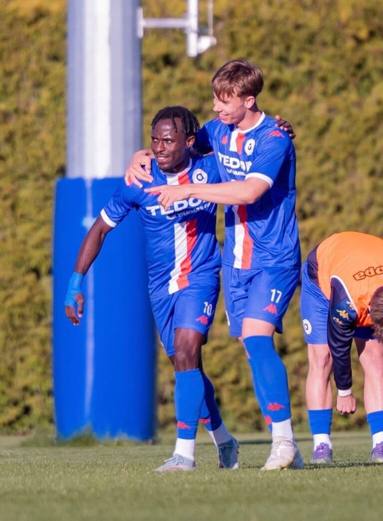 Two soccer players in blue uniforms celebrate together on the field, one with an arm around the other in a joyful moment.
