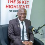 Smiling man in a dark suit sits in a podcast studio with a large microphone in front and a banner reading 'THE 36 KEY HIGHLIGHTS' in the background.