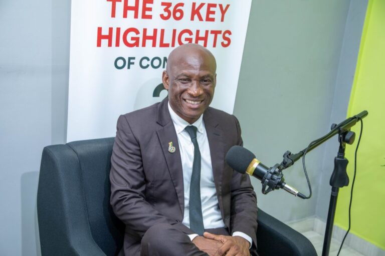 Smiling man in a dark suit sits in a podcast studio with a large microphone in front and a banner reading 'THE 36 KEY HIGHLIGHTS' in the background.