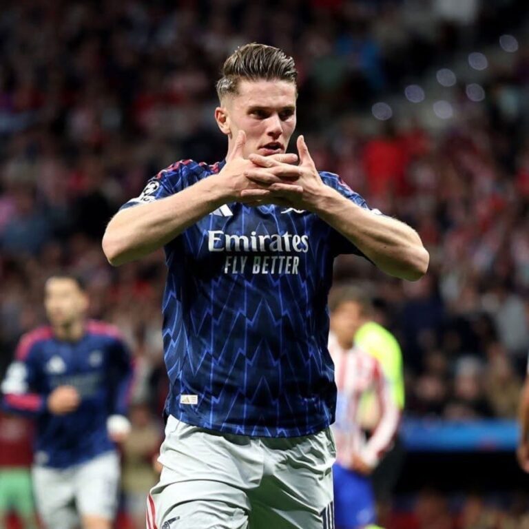 Soccer player in a blue Emirates jersey celebrating on the pitch, hands clasped in front of him.