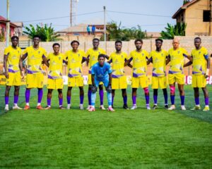Soccer team in yellow jerseys lined up on a green field, goalkeeper in blue kneeling at center for a team photo