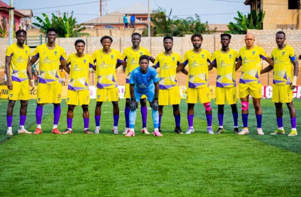 Soccer team in yellow jerseys lined up on a green field, goalkeeper in blue kneeling at center for a team photo