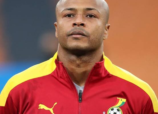 Head-and-shoulders portrait of a bald man wearing a red and yellow Ghana Football Association jacket, with the badge on the left chest, looking straight ahead.