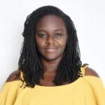 Portrait of a woman with braided hair wearing a yellow off-the-shoulder top, facing the camera against a white background.