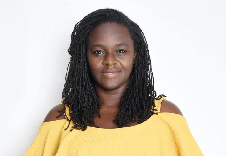 Portrait of a woman with braided hair wearing a yellow off-the-shoulder top, facing the camera against a white background.