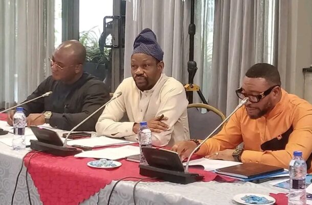 Panel of three men speaking at a conference table with microphones and tablets on the table.