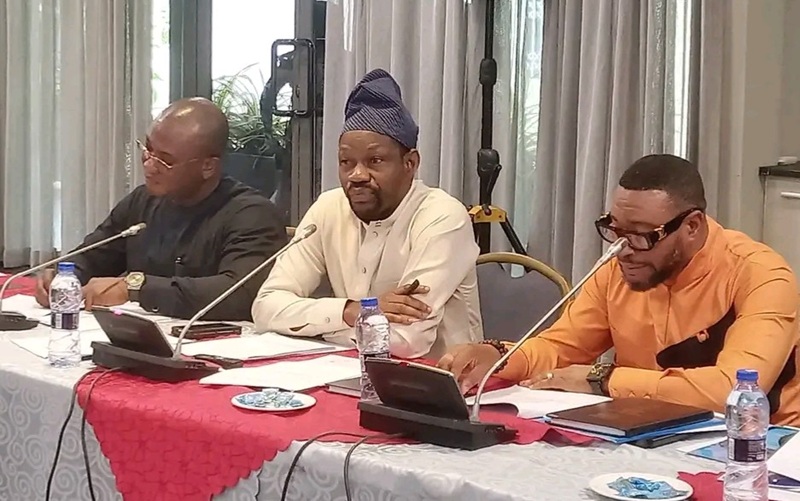 Panel of three men speaking at a conference table with microphones and tablets on the table.