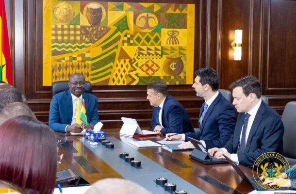 WhatsApp-Image-2026-04-29-at-22459-PM-1024x669 | Ghanaguardian.com Officials in suits sit around a long conference table in a wood-paneled room; a man on the left holds a small flag while others work on tablets and documents, with a colorful wall art and a Ministry of Finance seal in view.