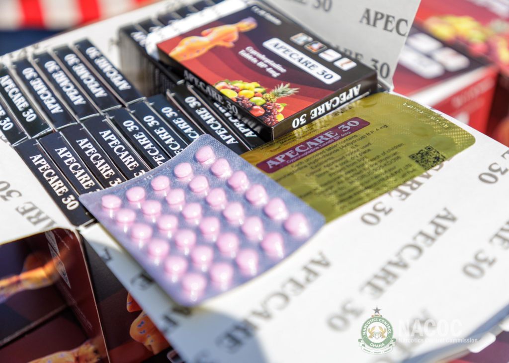 Assorted pharmaceutical boxes and pink blister pills piled together with a logo visible in the corner.