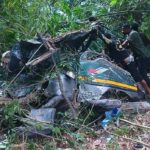 Two men salvage a damaged personal watercraft tangled in dense jungle vegetation after a crash.
