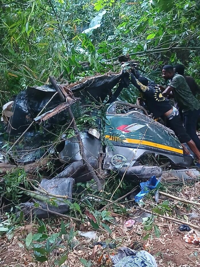 Two men salvage a damaged personal watercraft tangled in dense jungle vegetation after a crash.