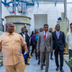 Group of officials on a factory tour walking past large industrial machinery in a processing plant.