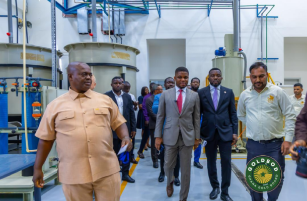 Group of officials on a factory tour walking past large industrial machinery in a processing plant.