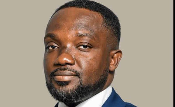 15198008 | Ghanaguardian.com Professional head-and-shoulders portrait of a Black man in a navy suit and white shirt, looking at the camera against a neutral beige background.