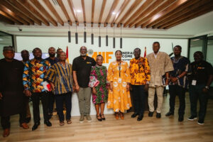 Group of fourteen people posing for a photo at an indoor event, some in colorful traditional African clothing, with a banner behind them.