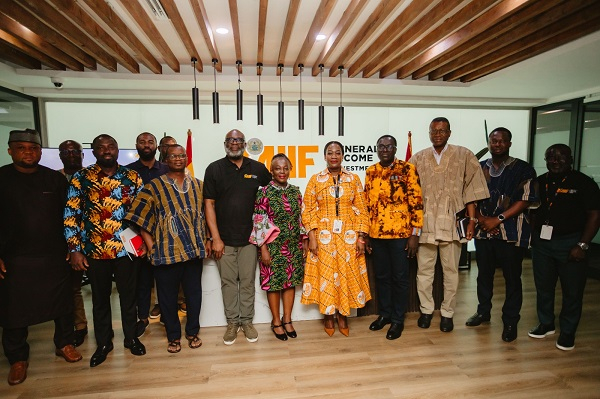 Group of fourteen people posing for a photo at an indoor event, some in colorful traditional African clothing, with a banner behind them.