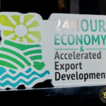 Sign promoting 24-Hour Economy and Accelerated Export Development; left side features a sun over green waves and stripes, with a small government seal in the corner (Ghana).