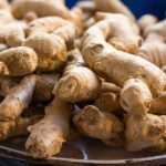 Pile of fresh ginger roots with knobby beige skin on a dark plate, ready for cooking.