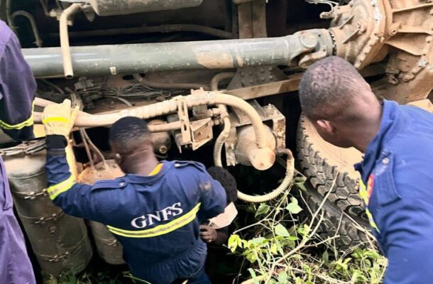700343708_994697449735875_2799267604736784620_n-1068x1424 | Ghanaguardian.com Rescuers in blue GNFS uniforms work beneath a large overturned truck, inspecting the undercarriage amid dirt and vegetation.