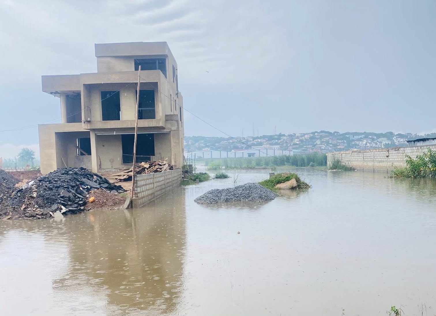 709769392_122173796150946649_9164639585945885179_n-e1779958968867 | Ghanaguardian.com Unfinished concrete building surrounded by floodwaters with piles of rubble and gravel nearby.