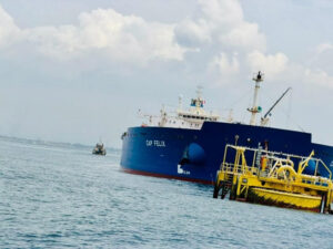 Large blue cargo ship named CAP FELIX beside a yellow offshore platform in calm sea waters.