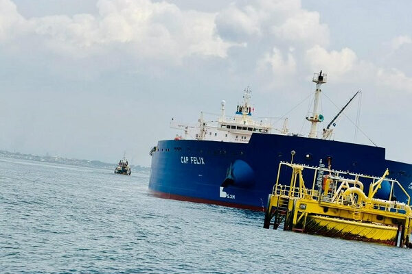 Large blue cargo ship named CAP FELIX beside a yellow offshore platform in calm sea waters.