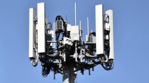 Cellular communication antenna array mounted on a pole against a blue sky, with multiple panel antennas and cables.