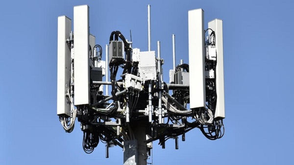 Cellular communication antenna array mounted on a pole against a blue sky, with multiple panel antennas and cables.