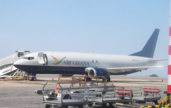 Air Ghana passenger jet parked on the tarmac beside ground support equipment and portable stairs at the gate.