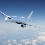 White passenger jet banking in the sky above a sea of clouds, blue clear backdrop