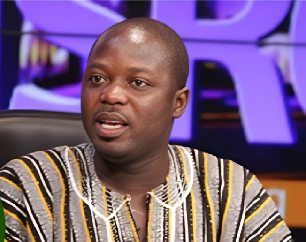Close-up of a man in a striped shirt speaking on a TV talk show set with a purple backdrop.