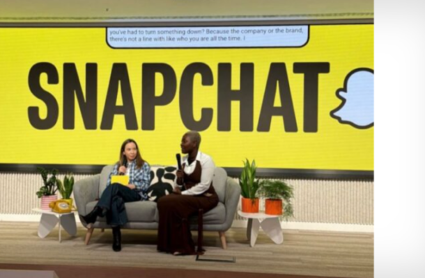 Two people sit on a sofa on stage with a huge Snapchat sign behind them, speaking into microphones.