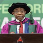 African man in purple academic gown and black mortarboard delivering a speech at a podium