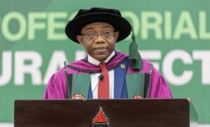 African man in purple academic gown and black mortarboard delivering a speech at a podium