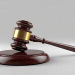 Judge's wooden gavel with a gold band resting on a round sound block.