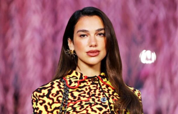 Model walking a fashion show wearing a yellow and black leopard‑print top against a pink blurred runway backdrop.