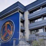 Exterior of the Ghana Police Command building with a blue facade and a circular seal on the front wall, gated entrance in the foreground.
