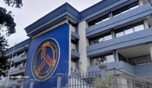 Exterior of the Ghana Police Command building with a blue facade and a circular seal on the front wall, gated entrance in the foreground.