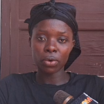 Woman with a black headwrap speaks into a microphone during an interview.
