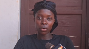 Woman with a black headwrap speaks into a microphone during an interview.