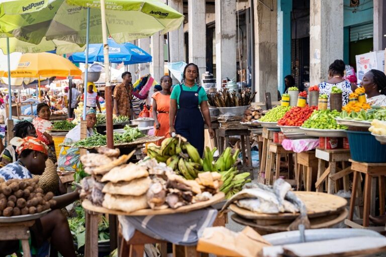 Busy outdoor market with stalls of fresh fruits and vegetables under colorful umbrellas.
