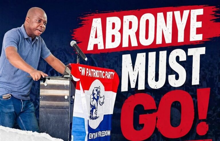 Man speaks at a political rally from behind a podium; a large sign behind him reads 'ABRONYE MUST GO!' in bold white and red letters.
